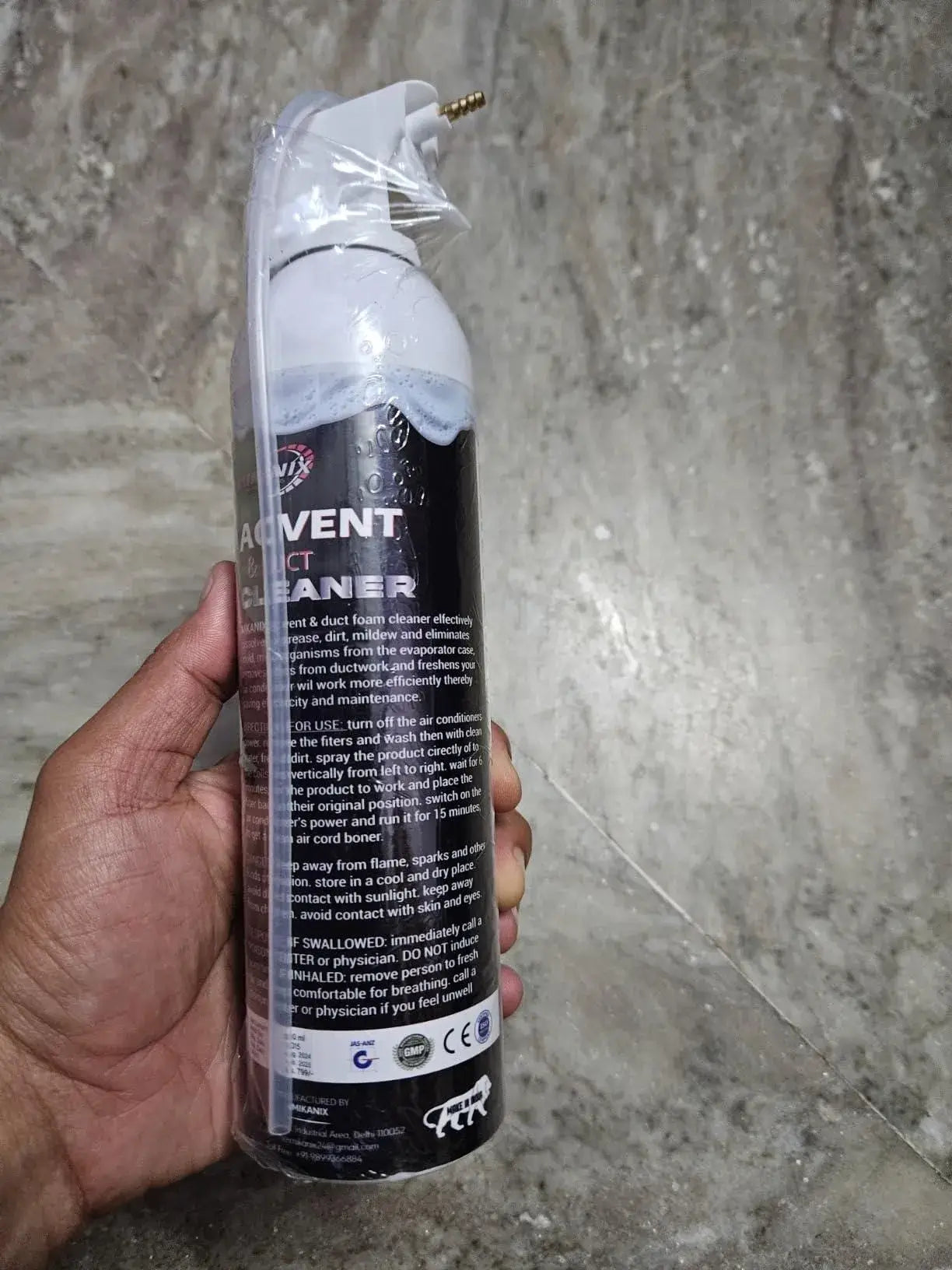 Hand holding a can of 'Vent' cleaner against a concrete wall background