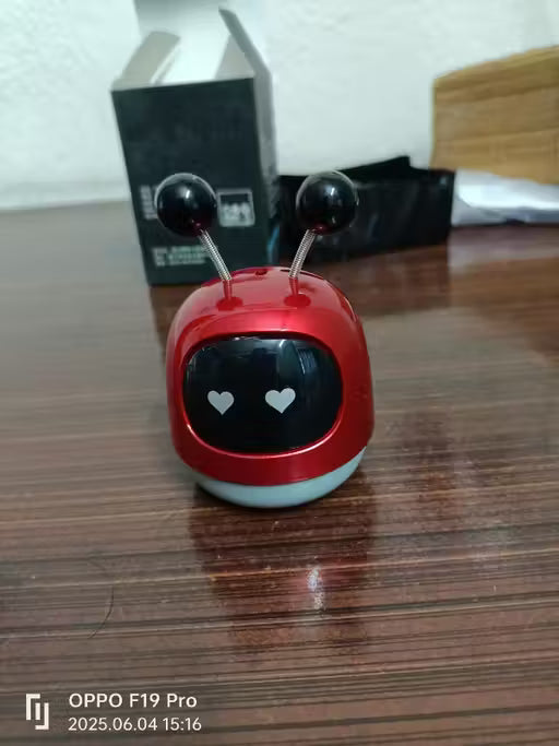 Small red robot toy with black eyes on a wooden surface