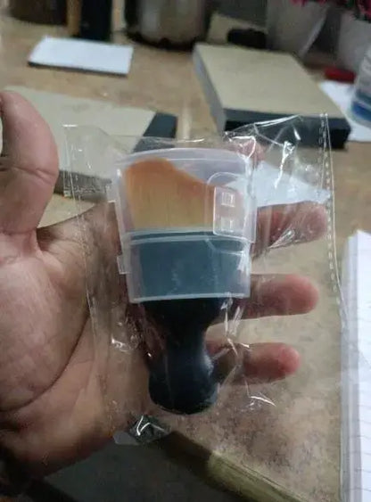 Hand holding a small plastic container with a brush inside, on a blurred background.