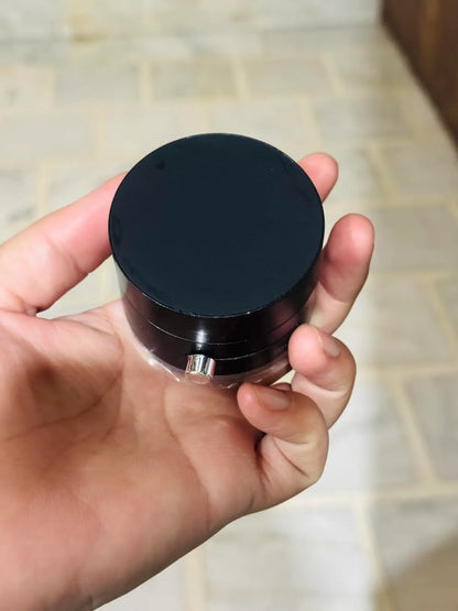 Hand holding a black round object with a reflective surface on a tiled floor background