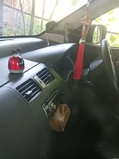 Car dashboard with a red car accessory and tassel hanging from the rearview mirror.