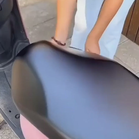 Person placing a premium waterproof bike seat cover on a pink scooter seat, showcasing its sleek design.