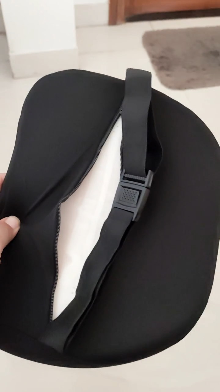 Black seat cover with a strap held by a hand on a white surface.